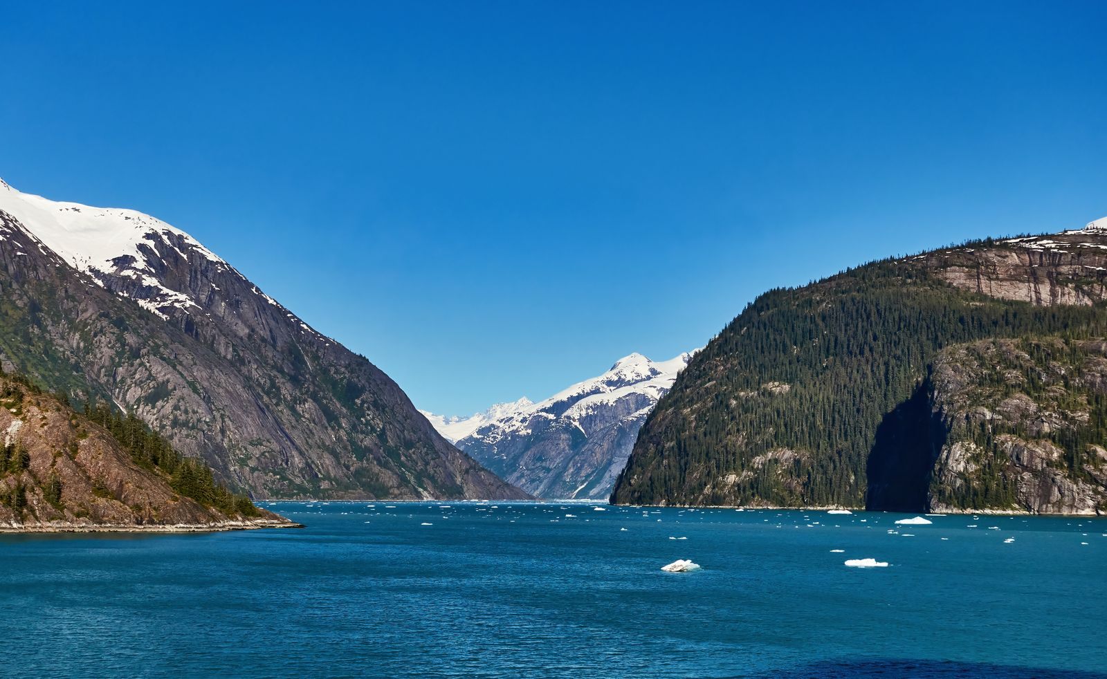 Steep green mountains and a snow-capped peak above a blue Alaskan fjord, the scenery of Christian cruises to Alaska