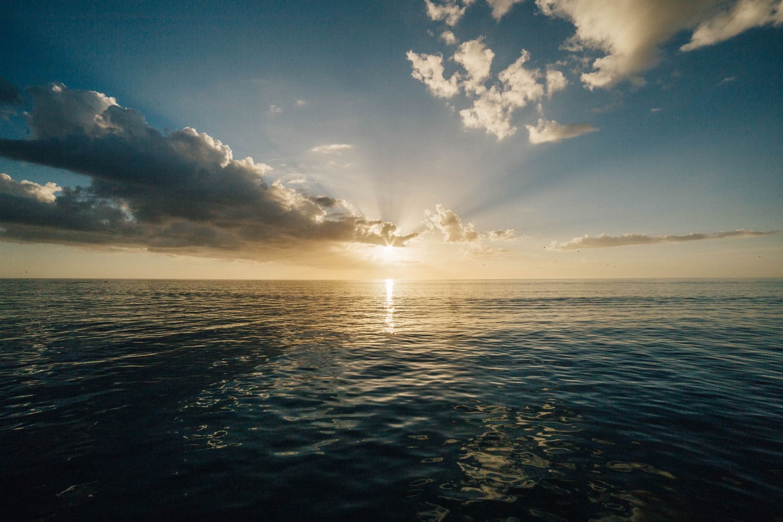 Sun rays breaking through clouds over a calm sea at dawn