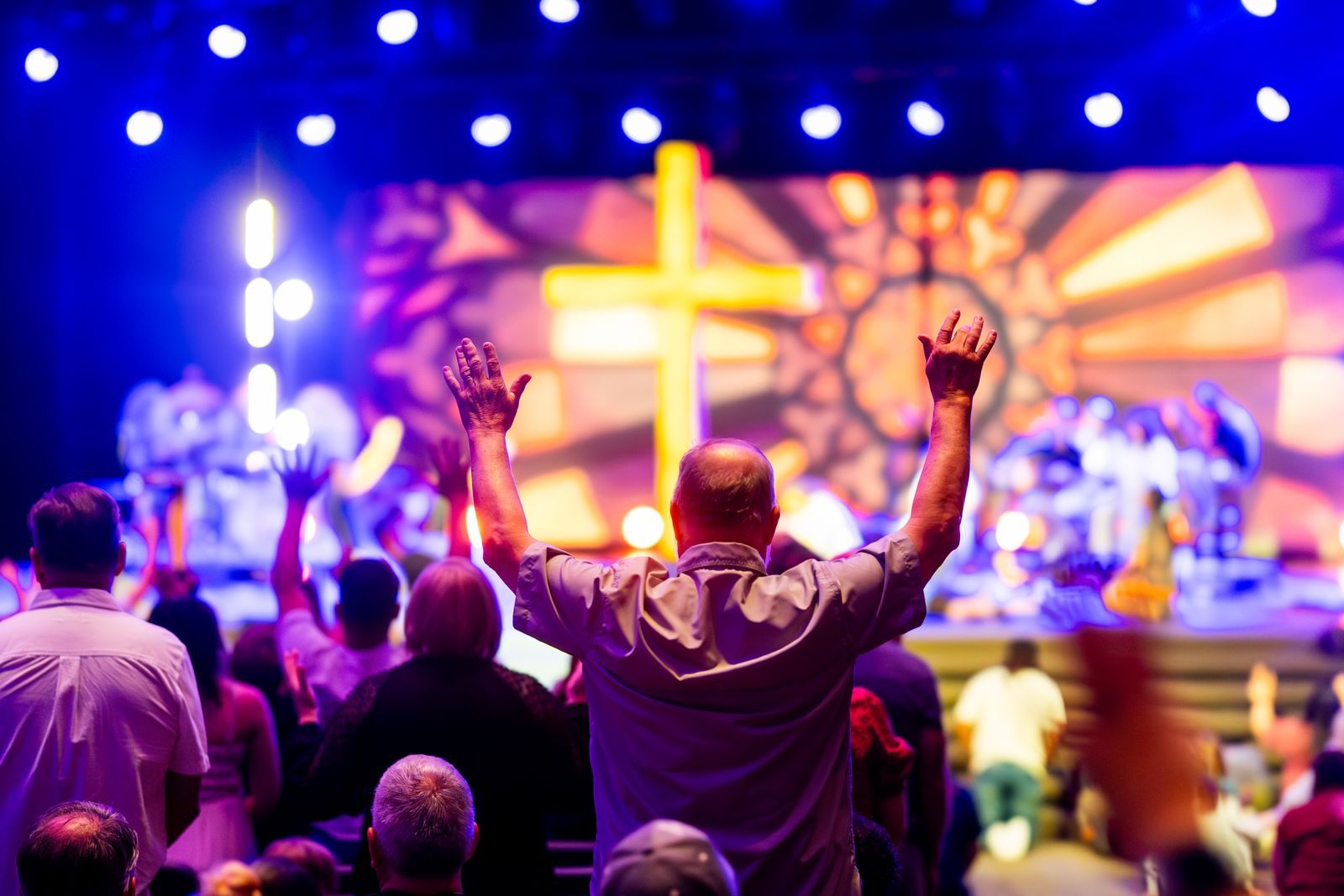 Worshipers raising their hands toward a lit cross on stage, the spirit of Christian cruises