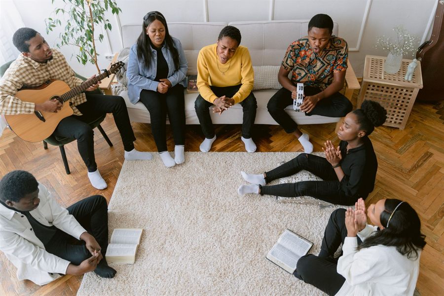 Small group singing and praying together in a living room with a guitar
