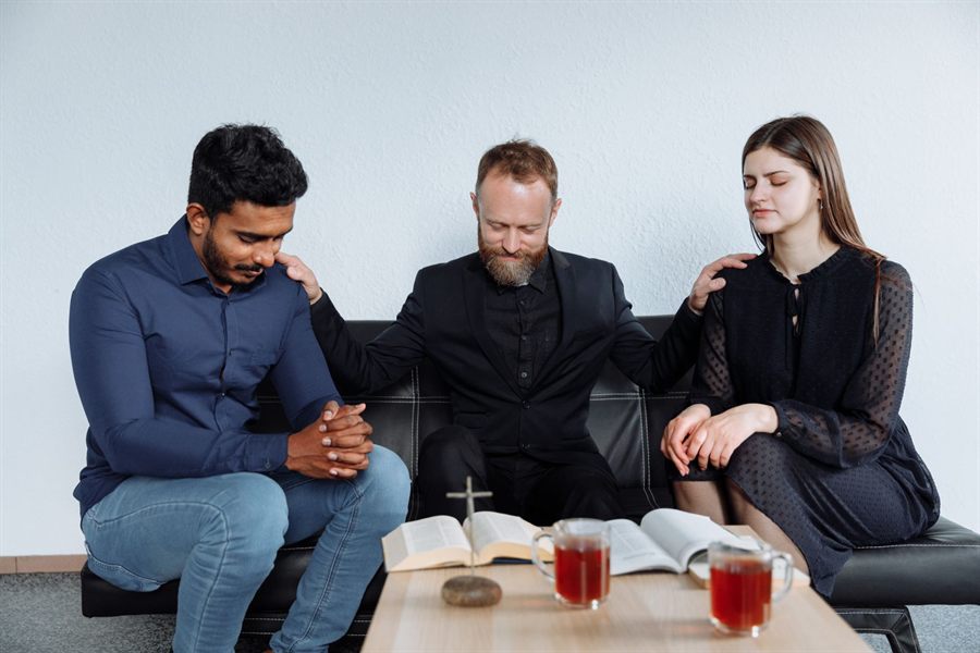 Three adults praying together with an open Bible on the table