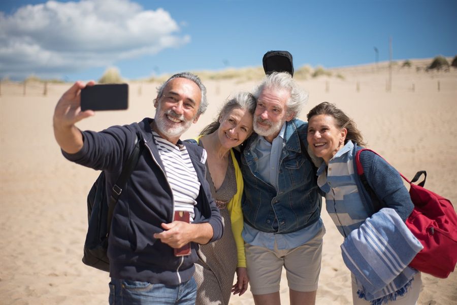 Group of older friends taking a selfie together on a sandy beach